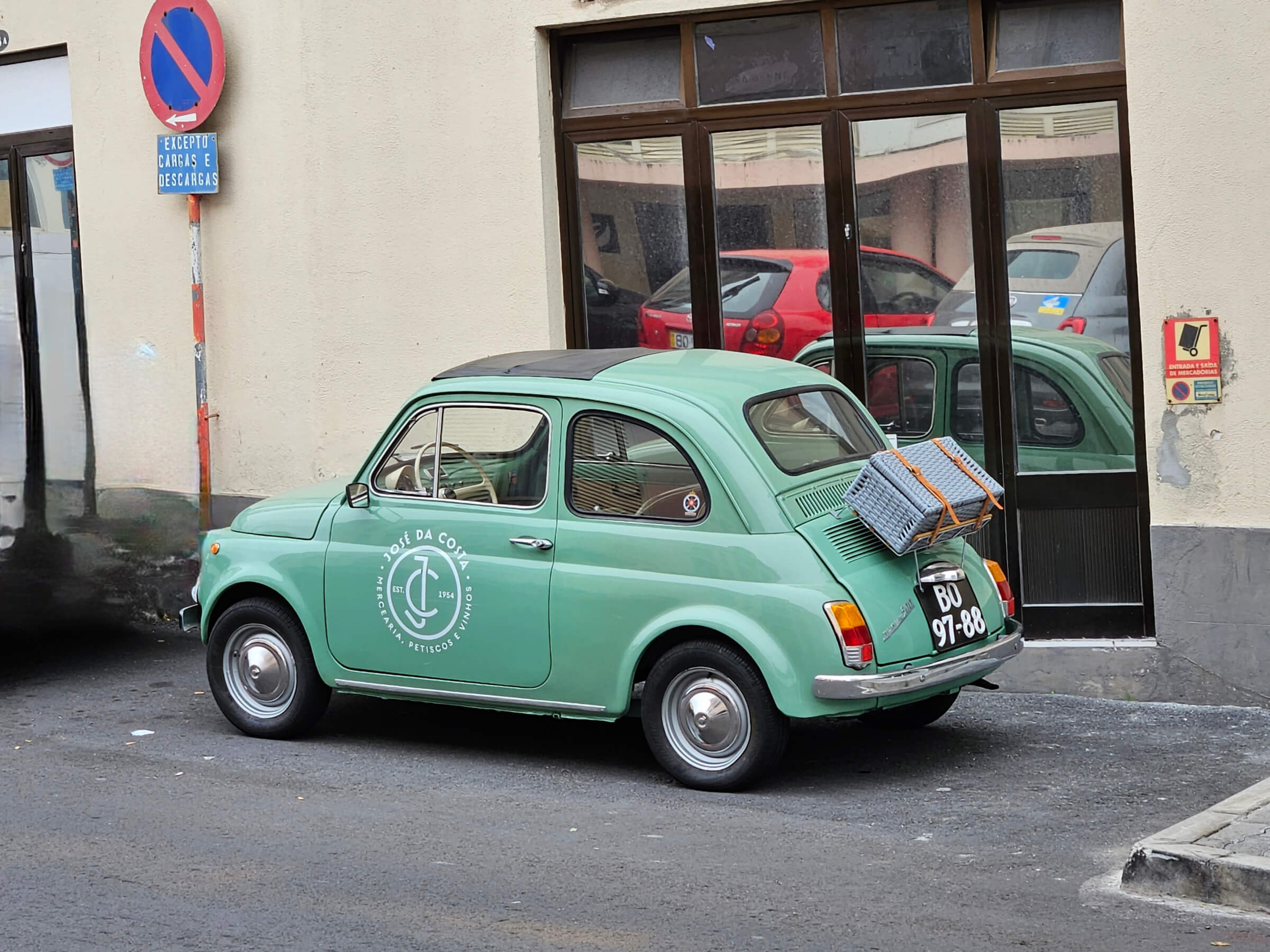 Ein mintgrüner Fiat 500 parkt an einer Straßenecke, mit einem Gitter auf dem Dach und gegenüberliegenden Spiegelungen.