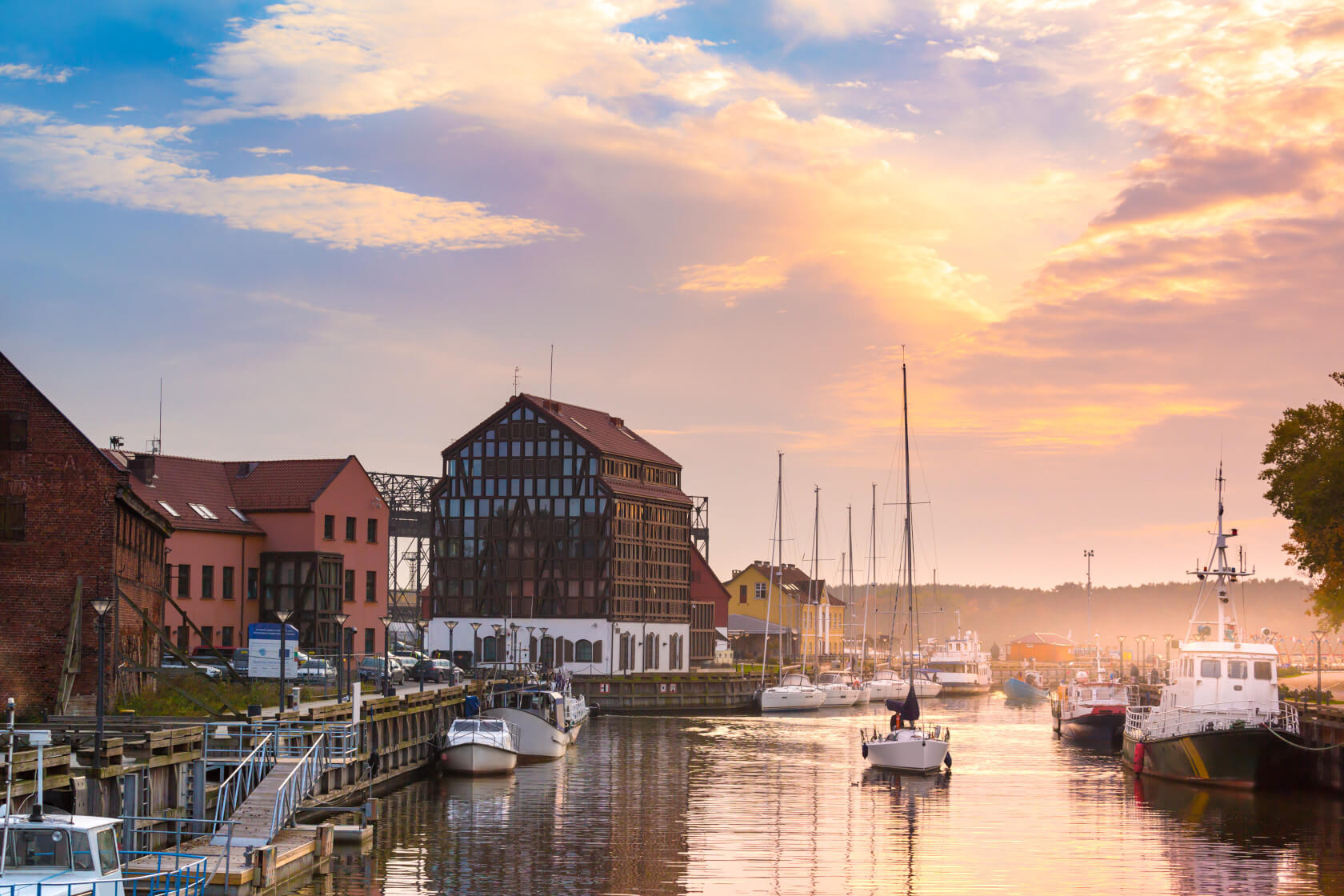 Hafenansicht bei Sonnenuntergang mit historischen Gebäuden und Segelbooten, die ruhig im Wasser liegen.
