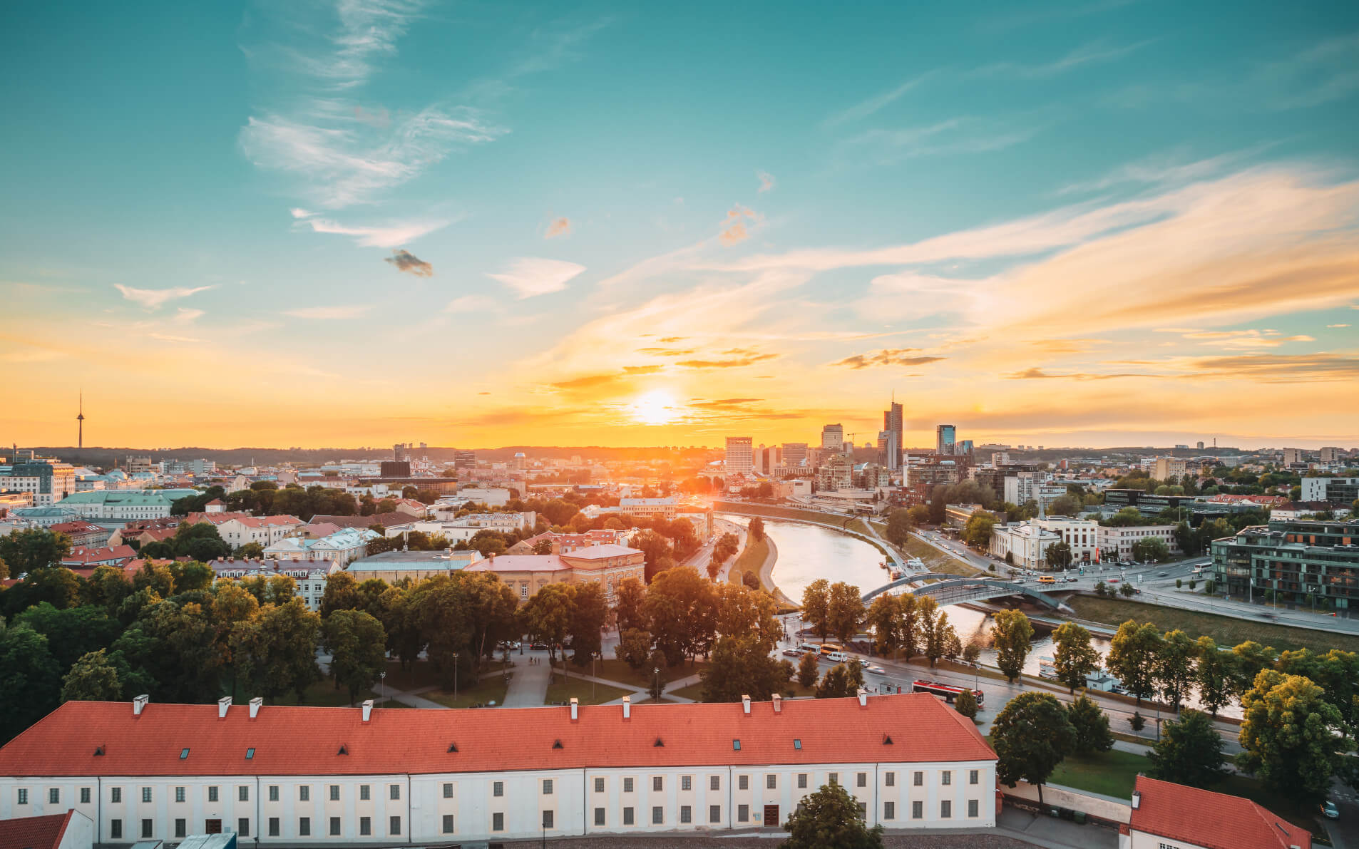 Sonnenuntergang über einer Stadt, Gebäude und Fluss sichtbar, warmes Licht und ein klarer Himmel im Hintergrund.