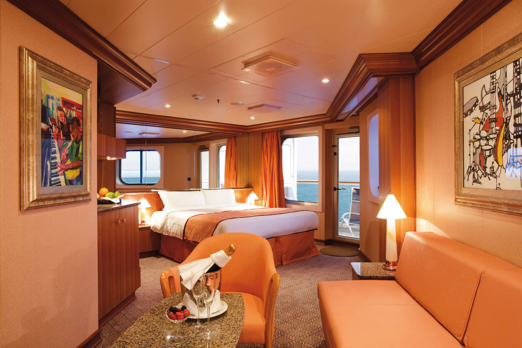 Eine helle Kabine mit Meerblick, großem Bett, Kunstwerken und gemütlicher Sitzecke, ideal zum Entspannen.