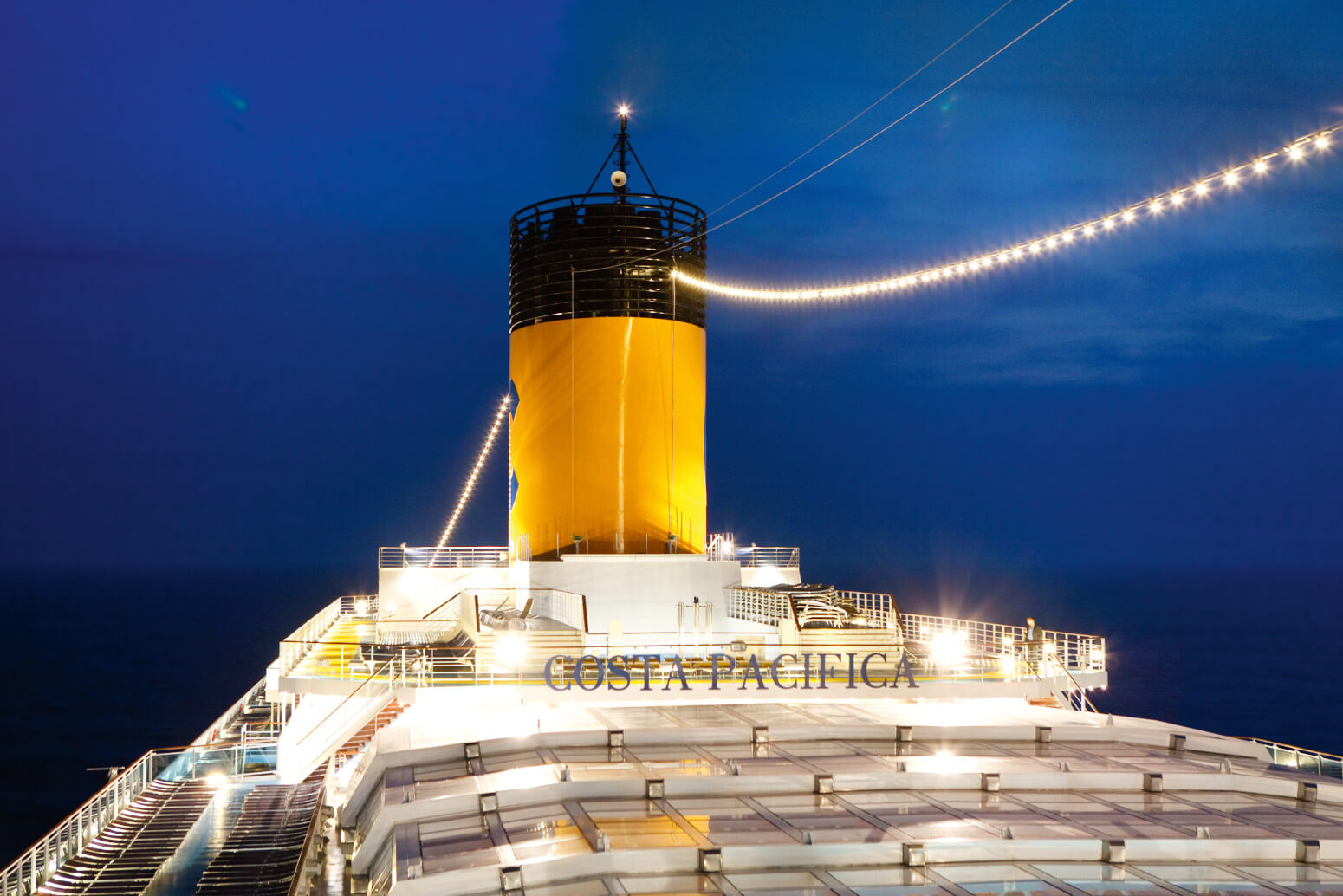 Das Bild zeigt den Schornstein des Kreuzfahrtschiffs Costa Pacifica bei Nacht, umgeben von ruhiger See.