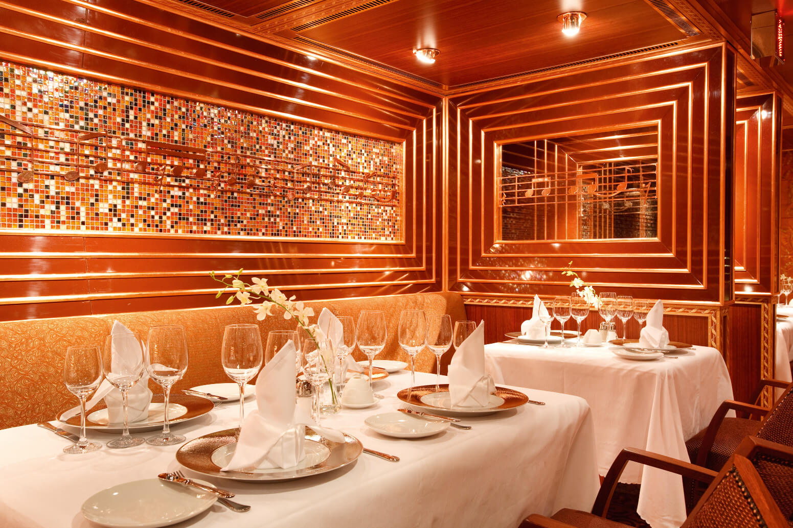 Elegantes Restaurant mit warmem Holzdesign, festlich gedeckten Tischen und einem mosaikartigen, musikalischen Wandbild.