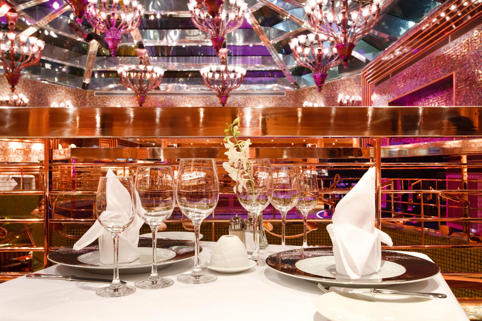 Eleganter Tisch im Restaurant mit Gläsern, Besteck und einem Blumenarrangement unter funkelnden Kronleuchtern.
