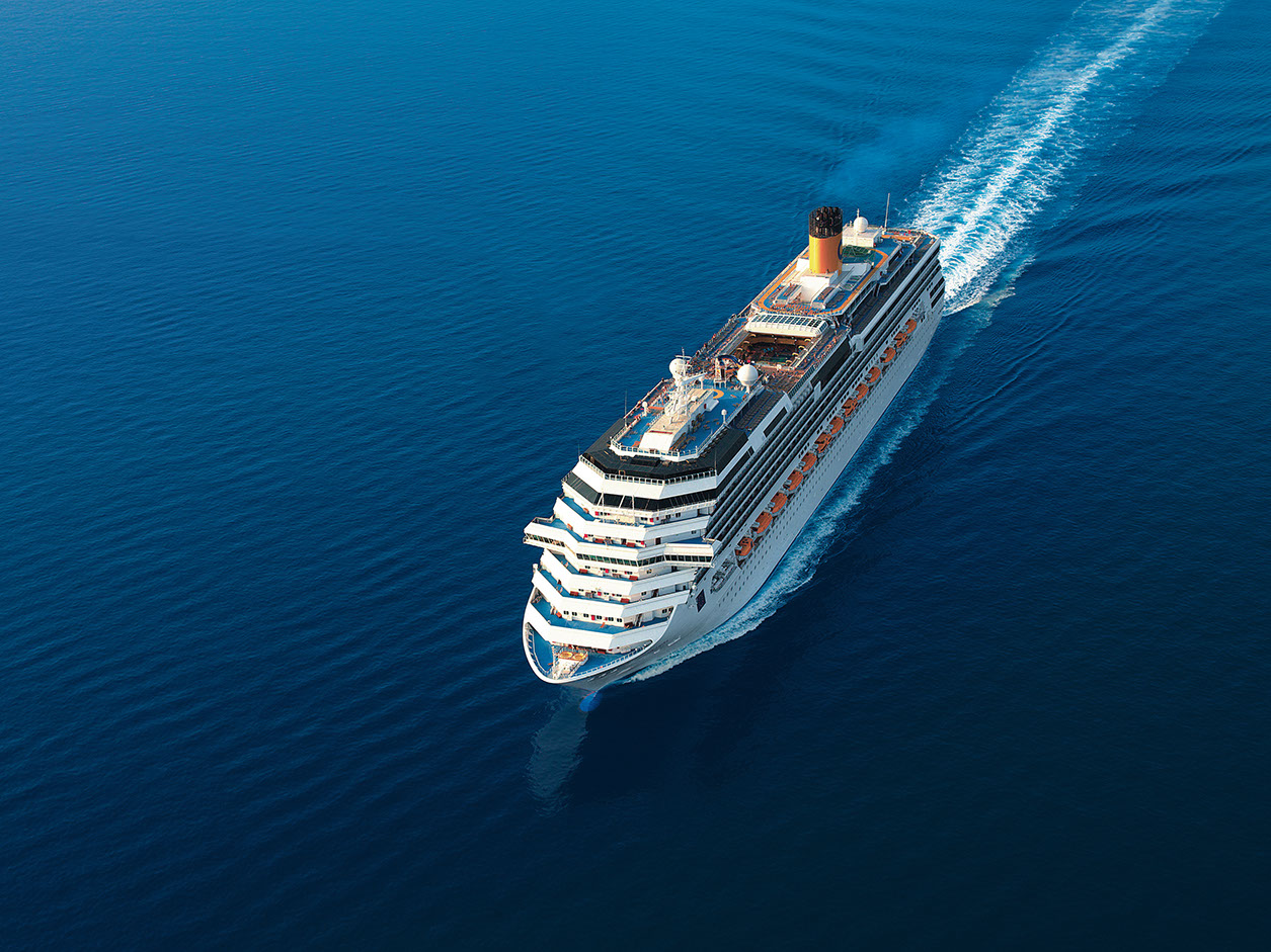 Ein großes Kreuzfahrtschiff fährt durch das tiefblaue Meer, hinterlässt eine sanfte Welle.