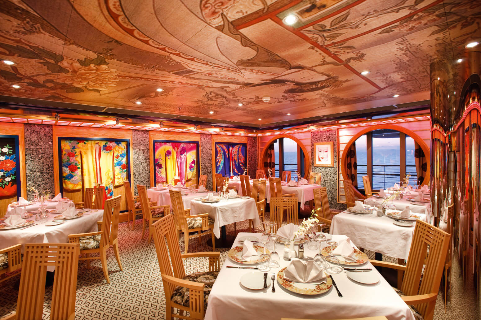 Elegantes Restaurant mit stilvollen Tischen, bunten Bildern und Meerblick durch große Fenster.