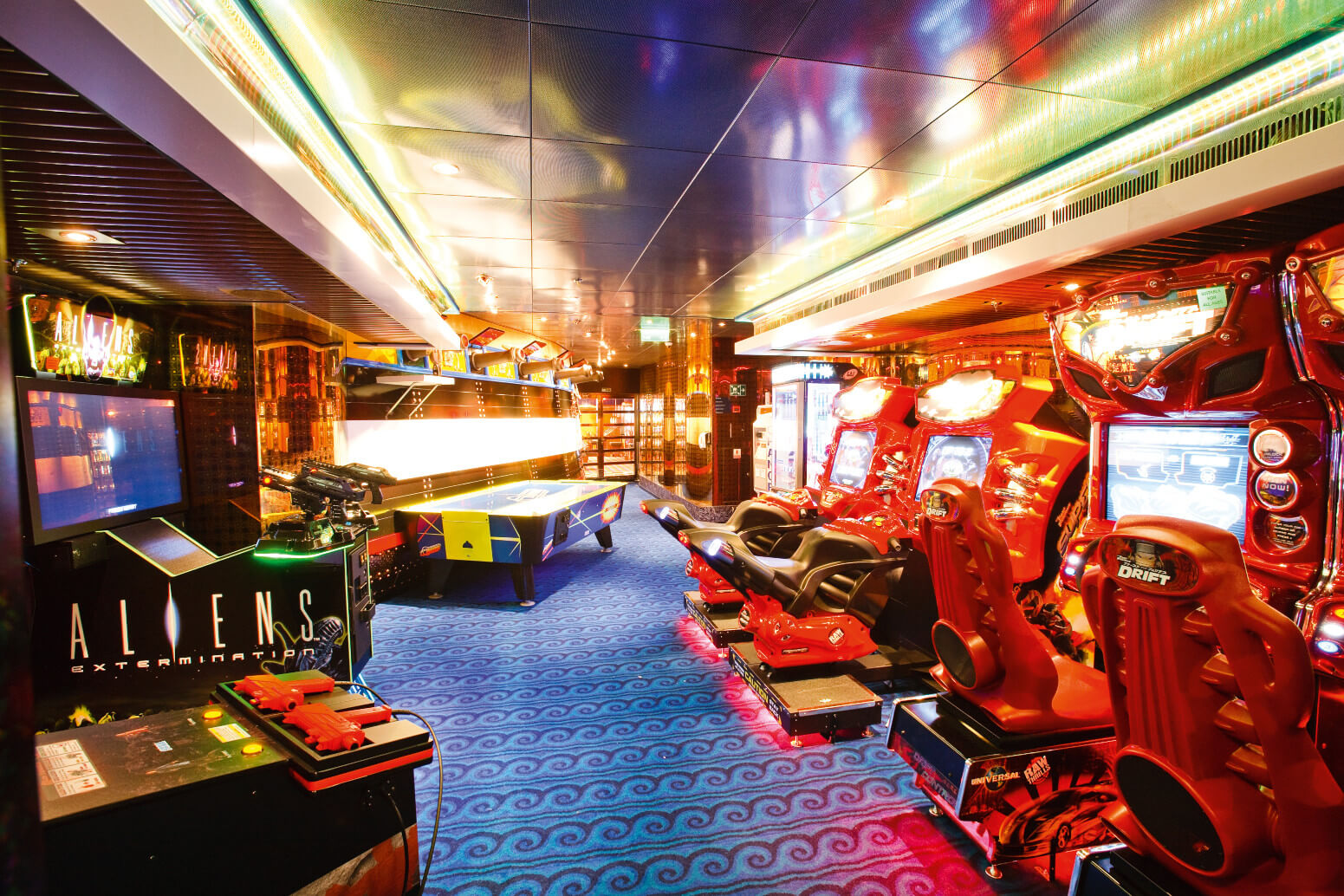 Ein lebendiger Innenraum mit Spielautomaten, Rennsport-Sesseln und bunten Lichtern auf einem blauen Teppichboden.