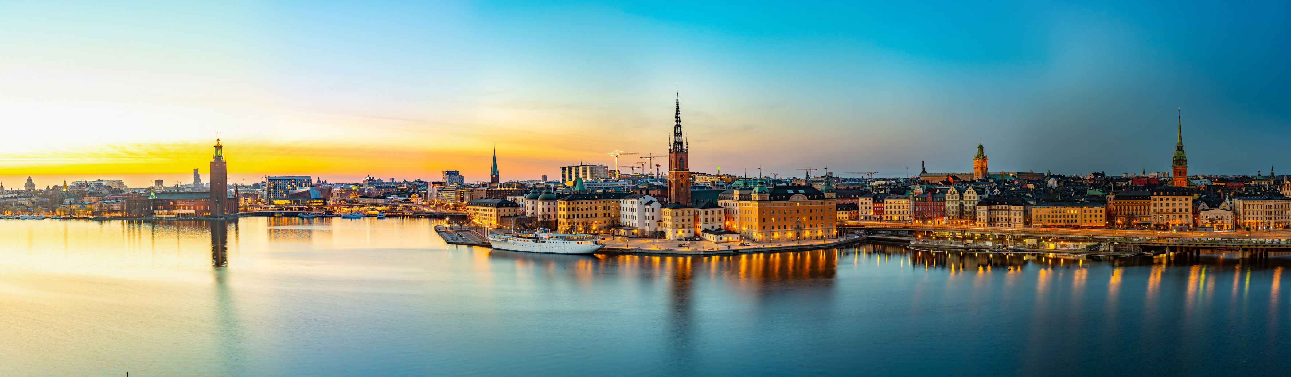 Ein Panorama von Stockholm bei Sonnenuntergang mit reflektierendem Wasser und leuchtenden Gebäuden.