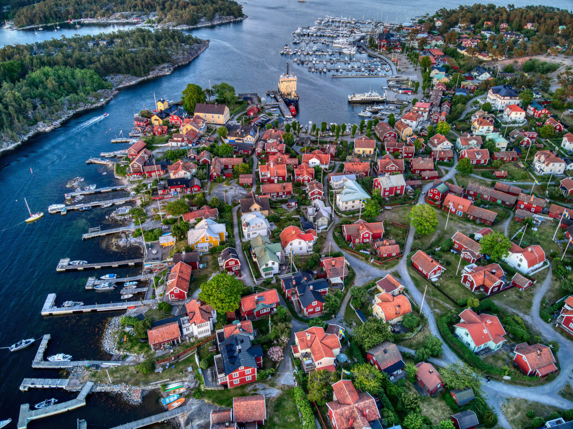 Eine malerische Küstenstadt mit roten Häusern, Yachten und grünen Bäumen, umgeben von hügeliger Landschaft.
