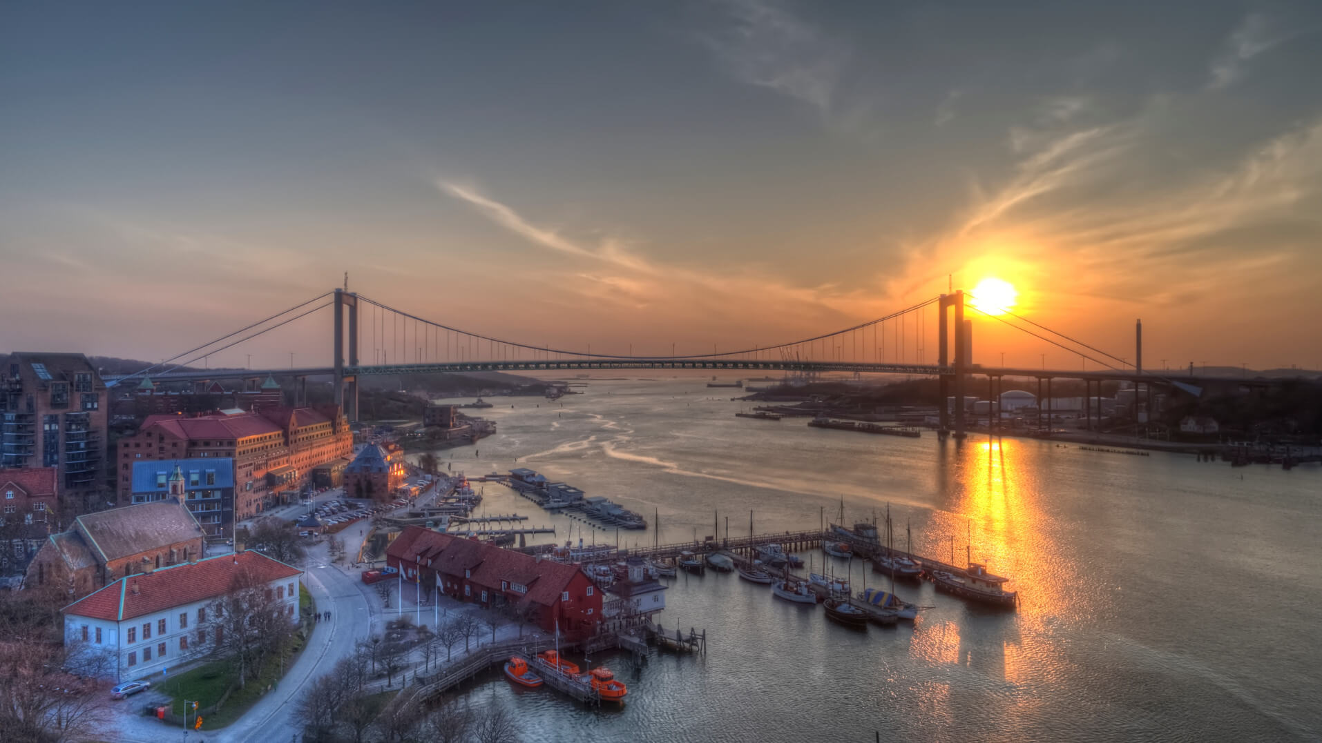 Sonnenuntergang über einem Fluss mit einer Brücke und Booten im Hafen, eine malerische Landschaft.