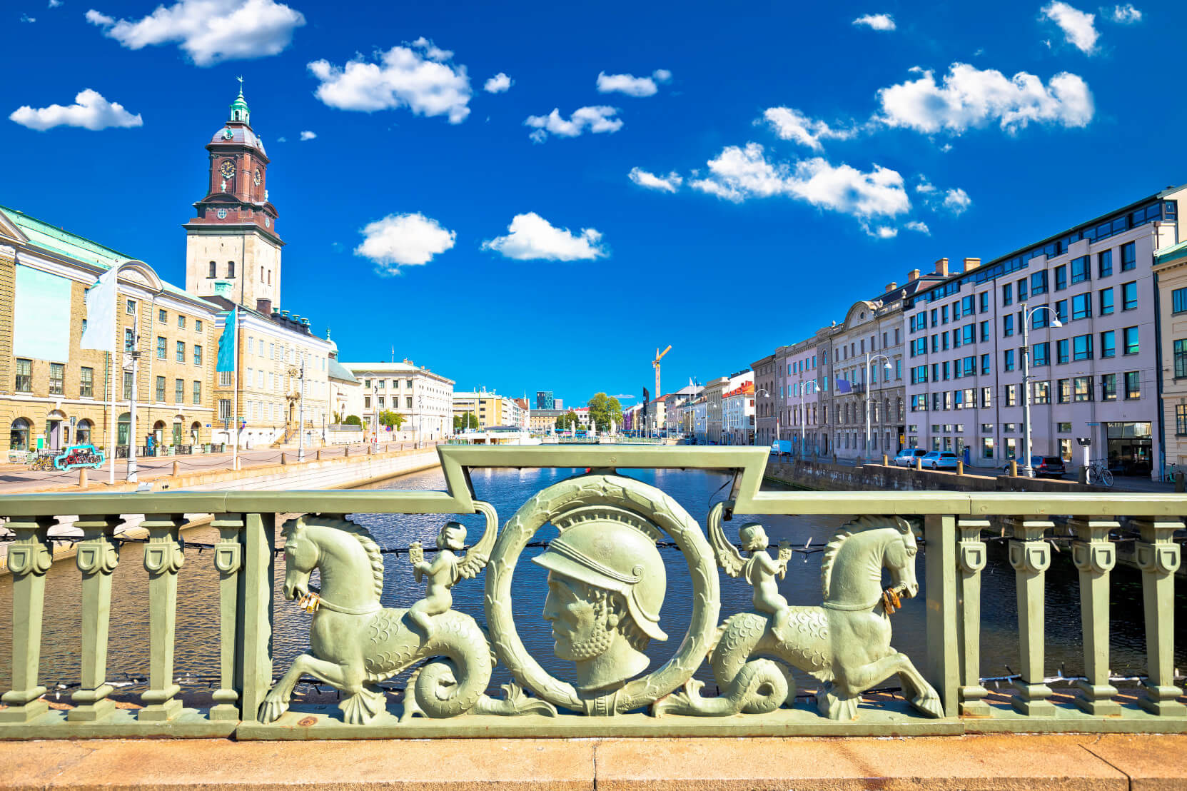 Eine Brücke mit kunstvollen Verzierungen, Blick auf Gebäude und Wasser unter klarem, blauem Himmel.