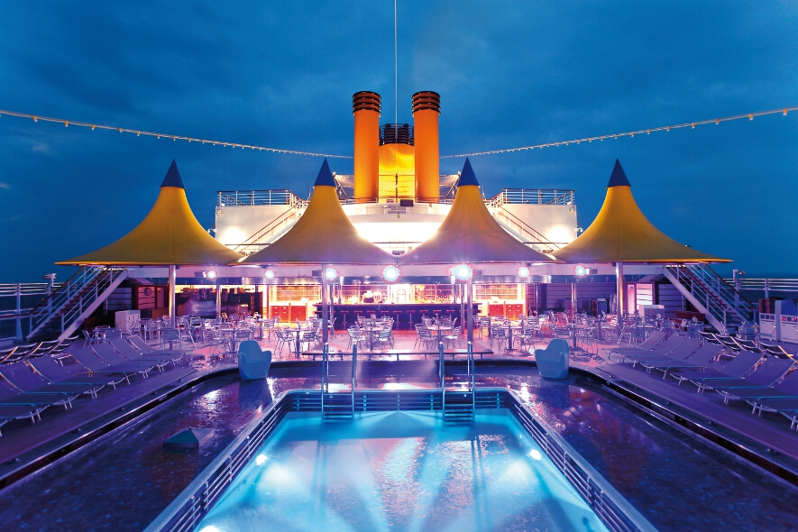 Ein Poolbereich auf einem Kreuzfahrtschiff mit bunten Zelten und stimmungsvollem Licht bei Dämmerung.