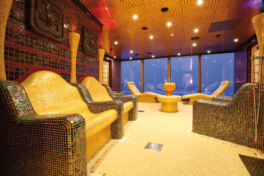 Ein stilvoller Wellnessbereich mit bunten Mosaikbänken und entspannendem Ambiente durch große Fenster.