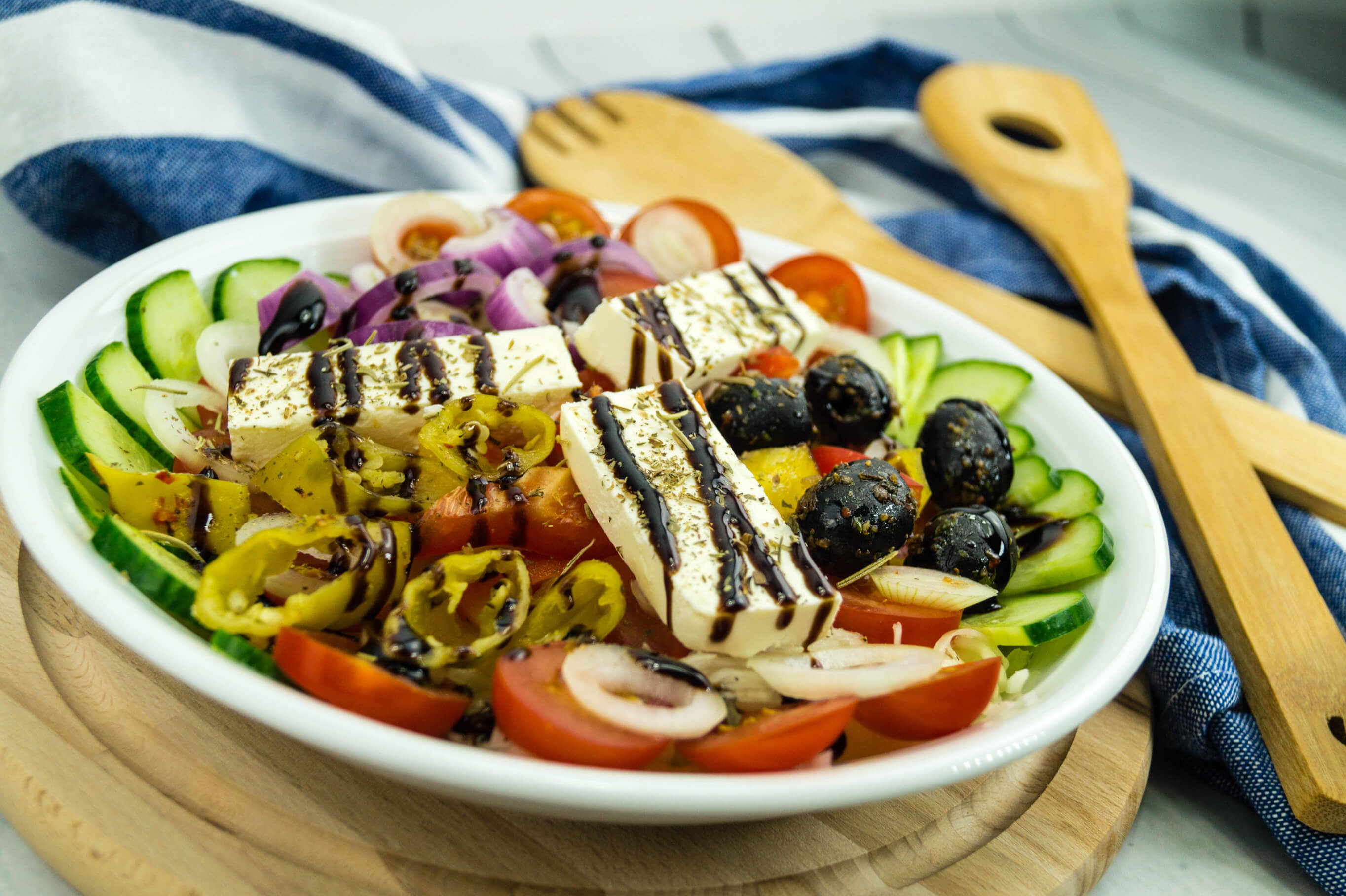 Bunte Salatschüssel mit Gurken, Tomaten, Zwiebeln, Oliven, Peperoni und Feta, serviert auf einem Holzbrett.