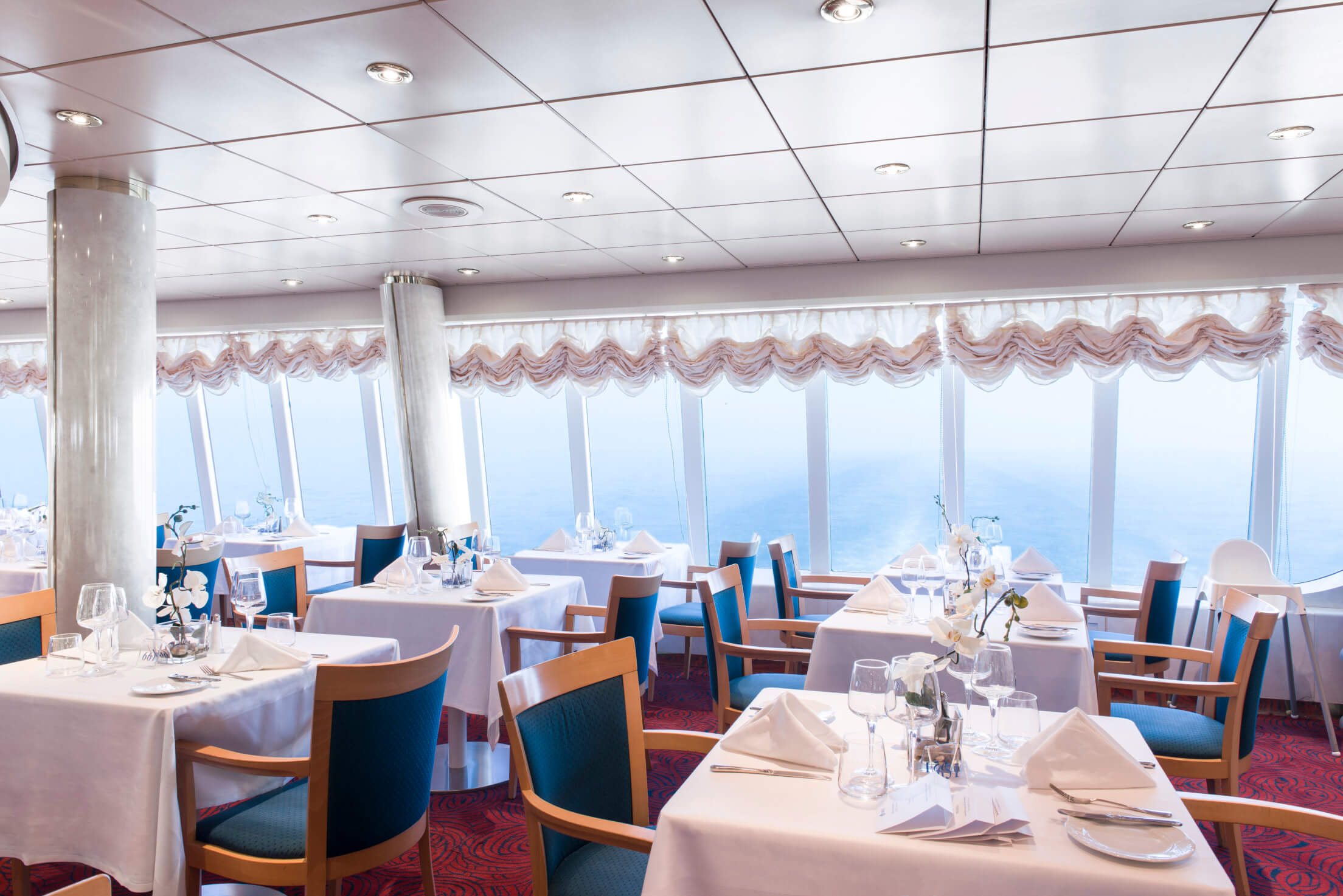 Elegantes Restaurant mit Meerblick, weißen Tischtüchern und modernen Möbeln, gemütliche Atmosphäre und Dekoration.