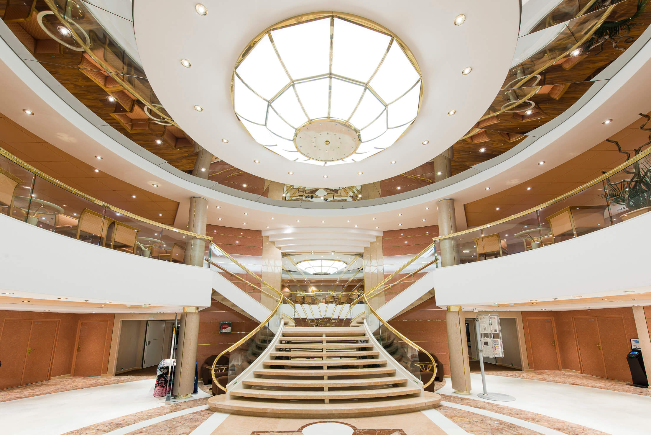 Elegante Treppe in einer stilvollen Halle mit runder Deckenbeleuchtung und gläsernen Geländern.