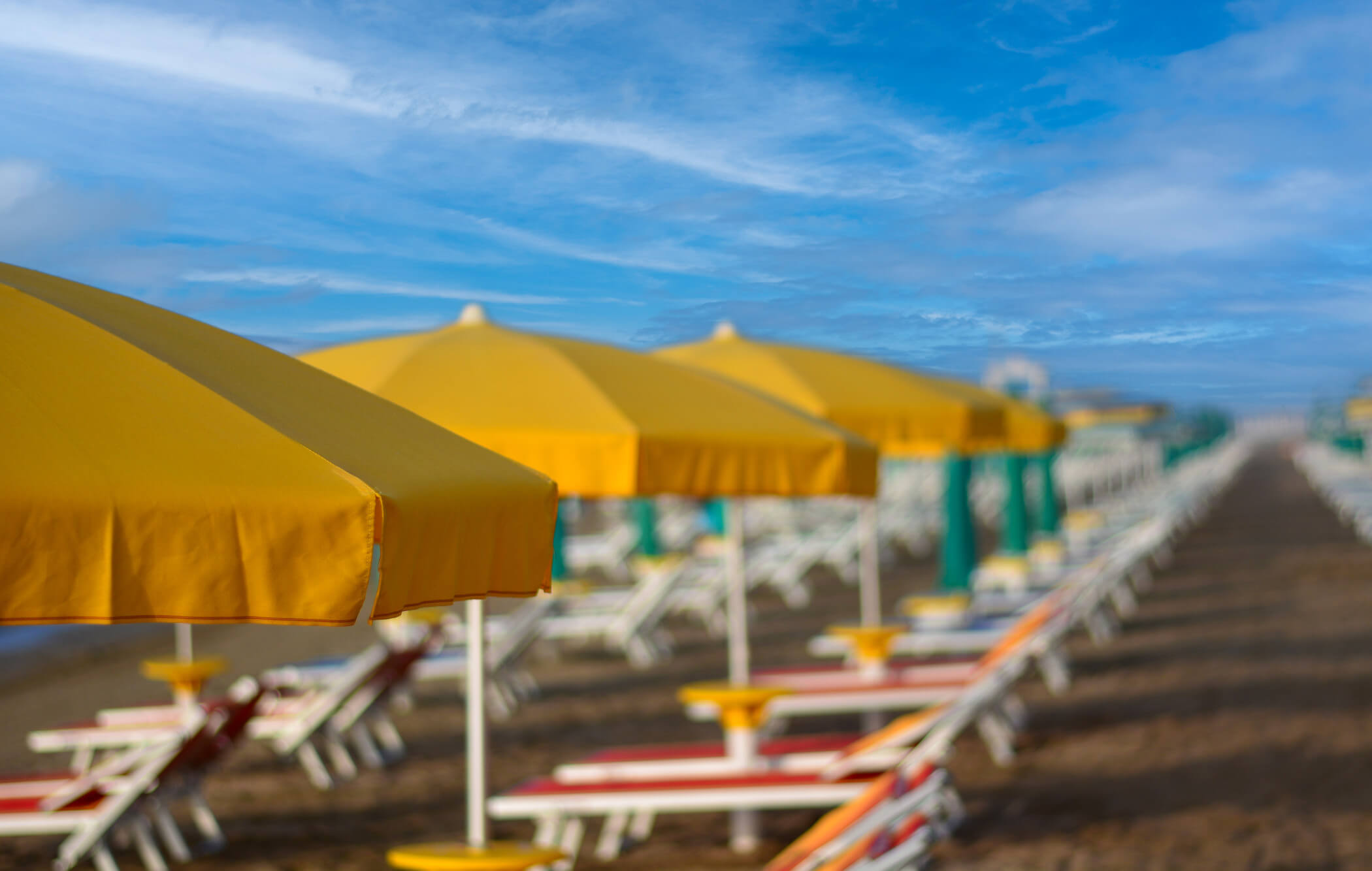Gelbe Sonnenschirme stehen in einer Reihe am Strand, umgeben von Liegen und einem klaren blauen Himmel.
