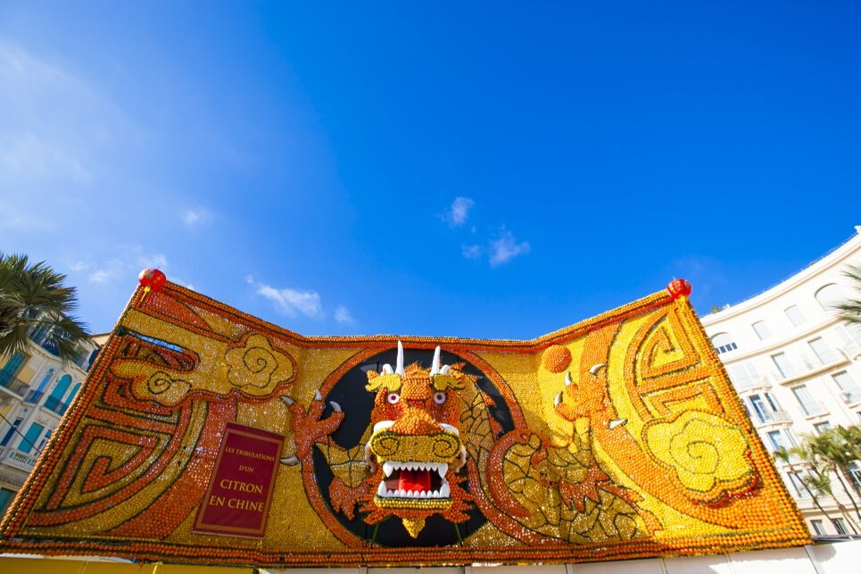 Eine bunte Dracheninstallation aus Zitrusfrüchten vor klarem Himmel, die eine Festivität darstellt.