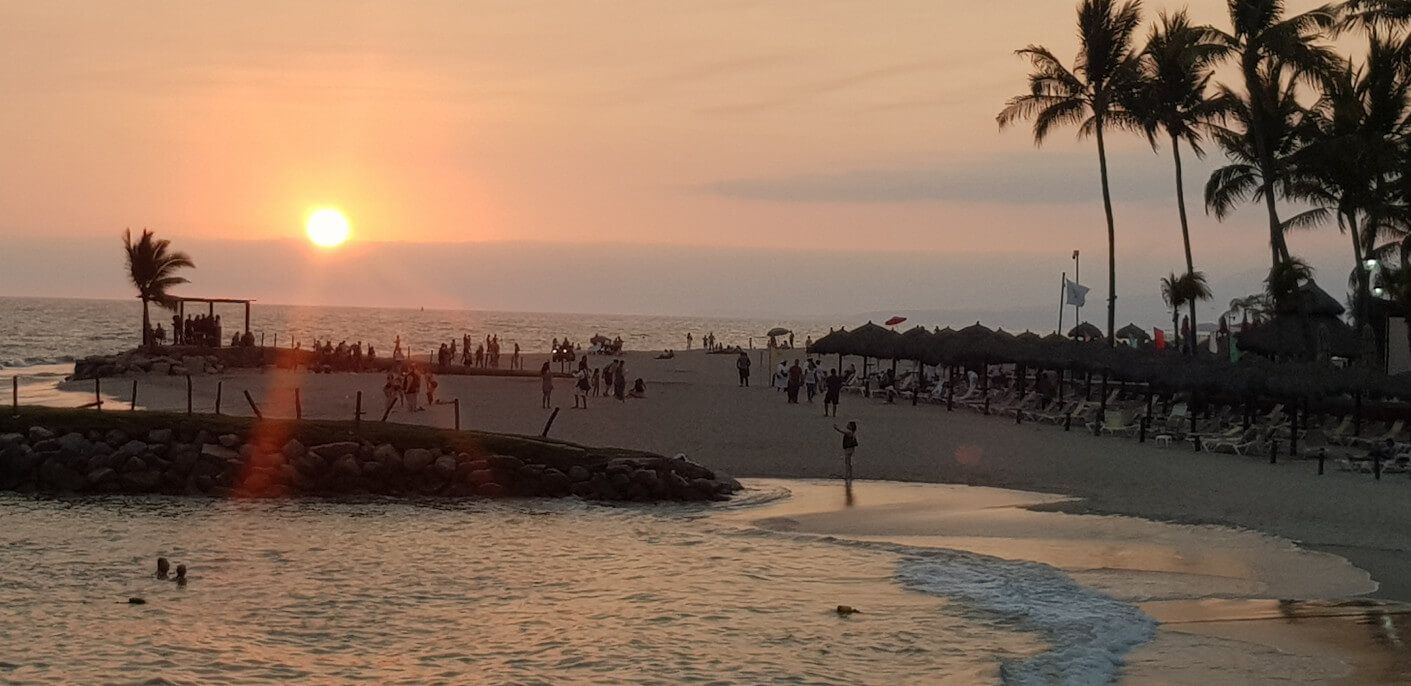 Schöner Sonnenuntergang am Strand mit Palmen und Menschen, die den Abend genießen. Entspannung pur!