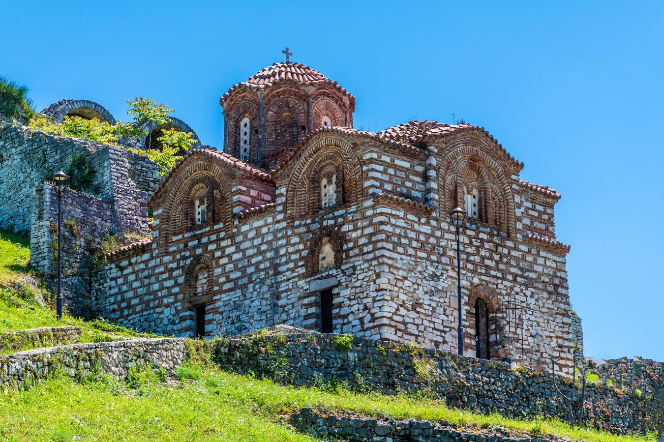 Eine historische Kirche mit Ziegelmuster, umgeben von grünen Wiesen und blauen Himmel.