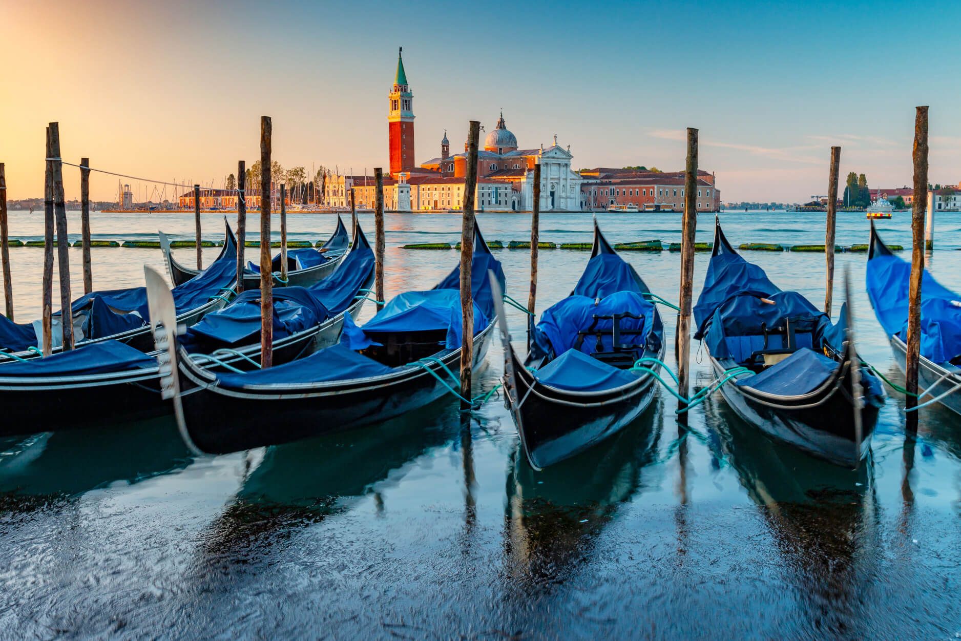 Venezianische Gondeln liegen ruhig im Wasser, mit der beeindruckenden Kulisse von Gebäuden und einem Turm im Hintergrund.