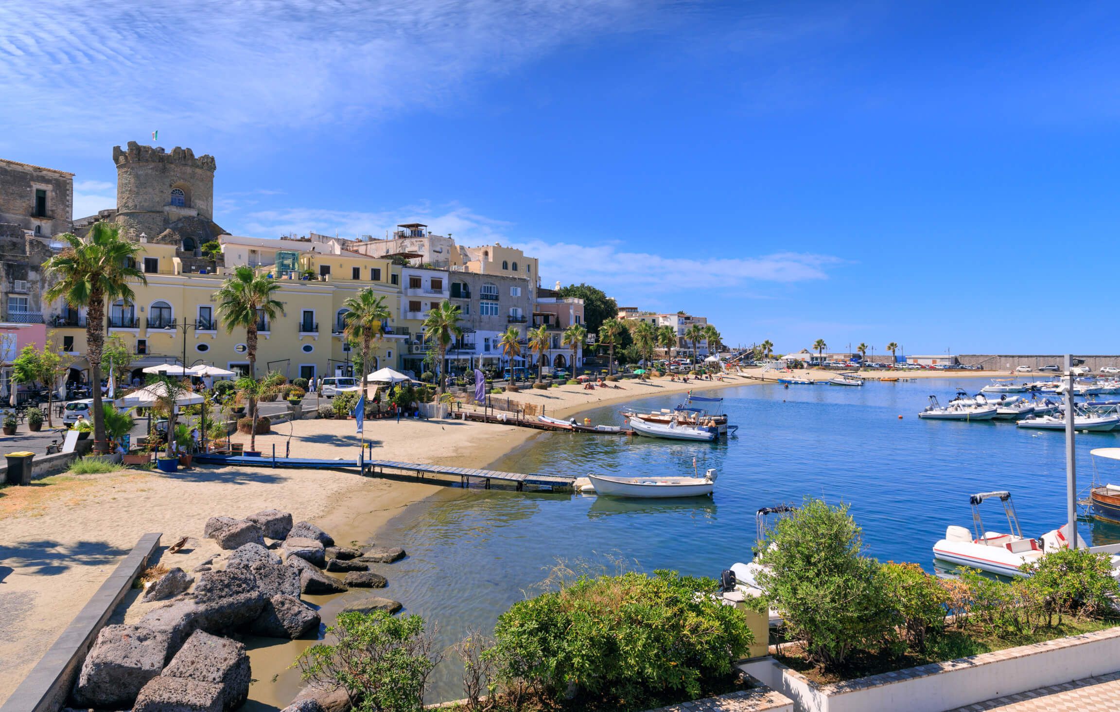 Ein malerischer Hafen mit Palmen, Sandstrand und Booten unter blauem Himmel. Ideal für einen entspannten Tag.