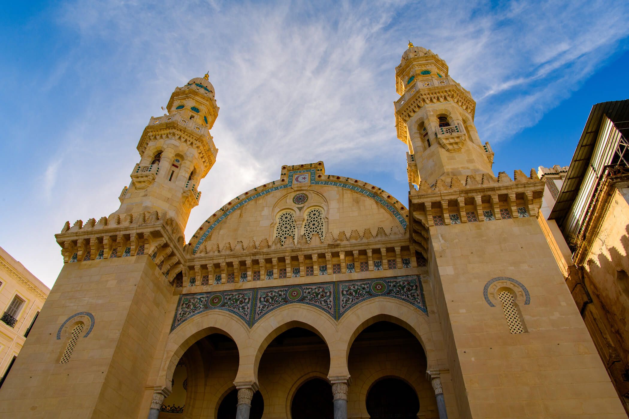 Eine beeindruckende Moschee mit eleganten Türmen und kunstvollen Ornamenten vor einem strahlend blauen Himmel.