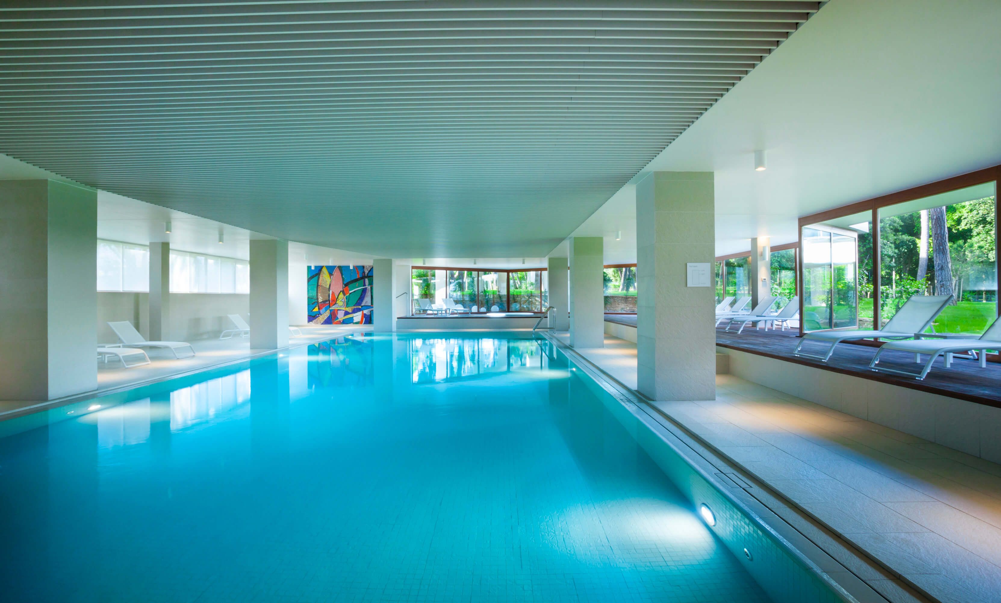 Ein eleganter Innenpool mit klarem Wasser, umgeben von großen Fenstern und modernen Liegen. Entspannung pur!