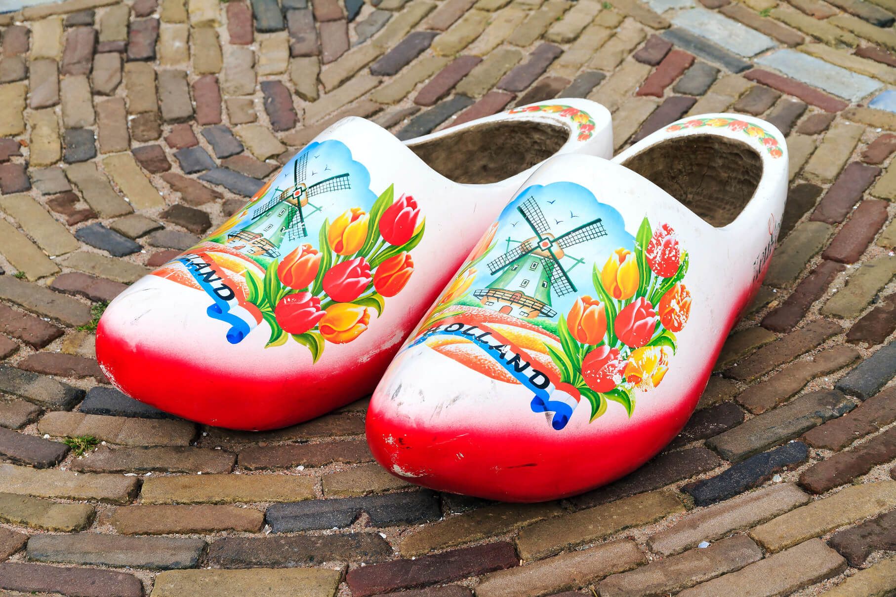Traditionelle holländische Holzschuhe mit bunten Blumen und Windmühlenmustern auf einem gepflasterten Boden.