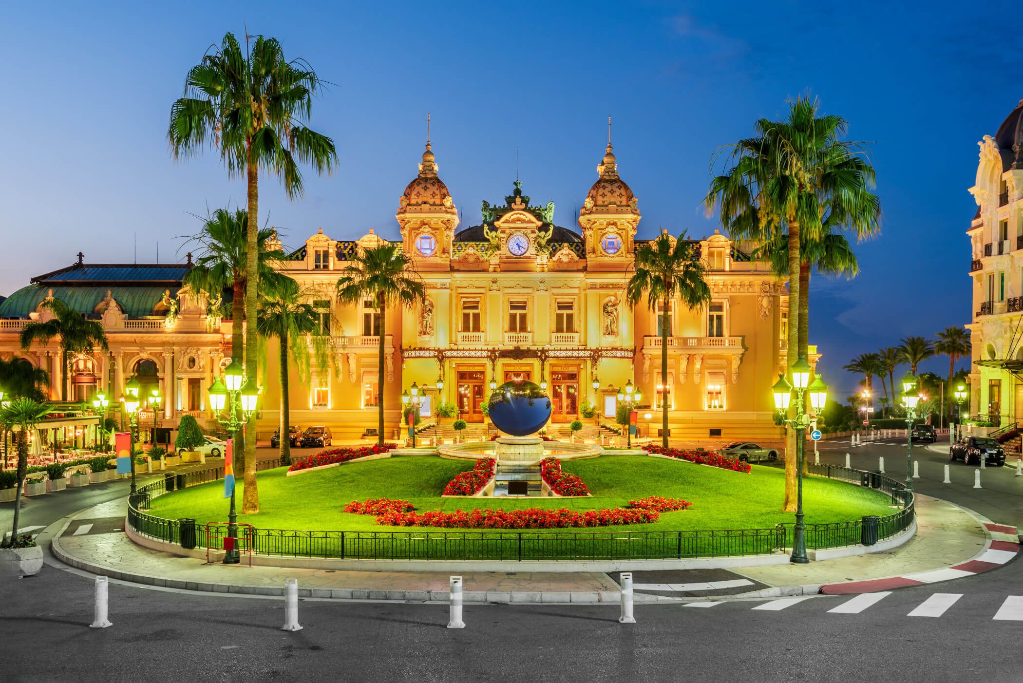 Das imposante Casino von Monte Carlo leuchtet in warmen Farben, umgeben von Palmen und schönem Garten.