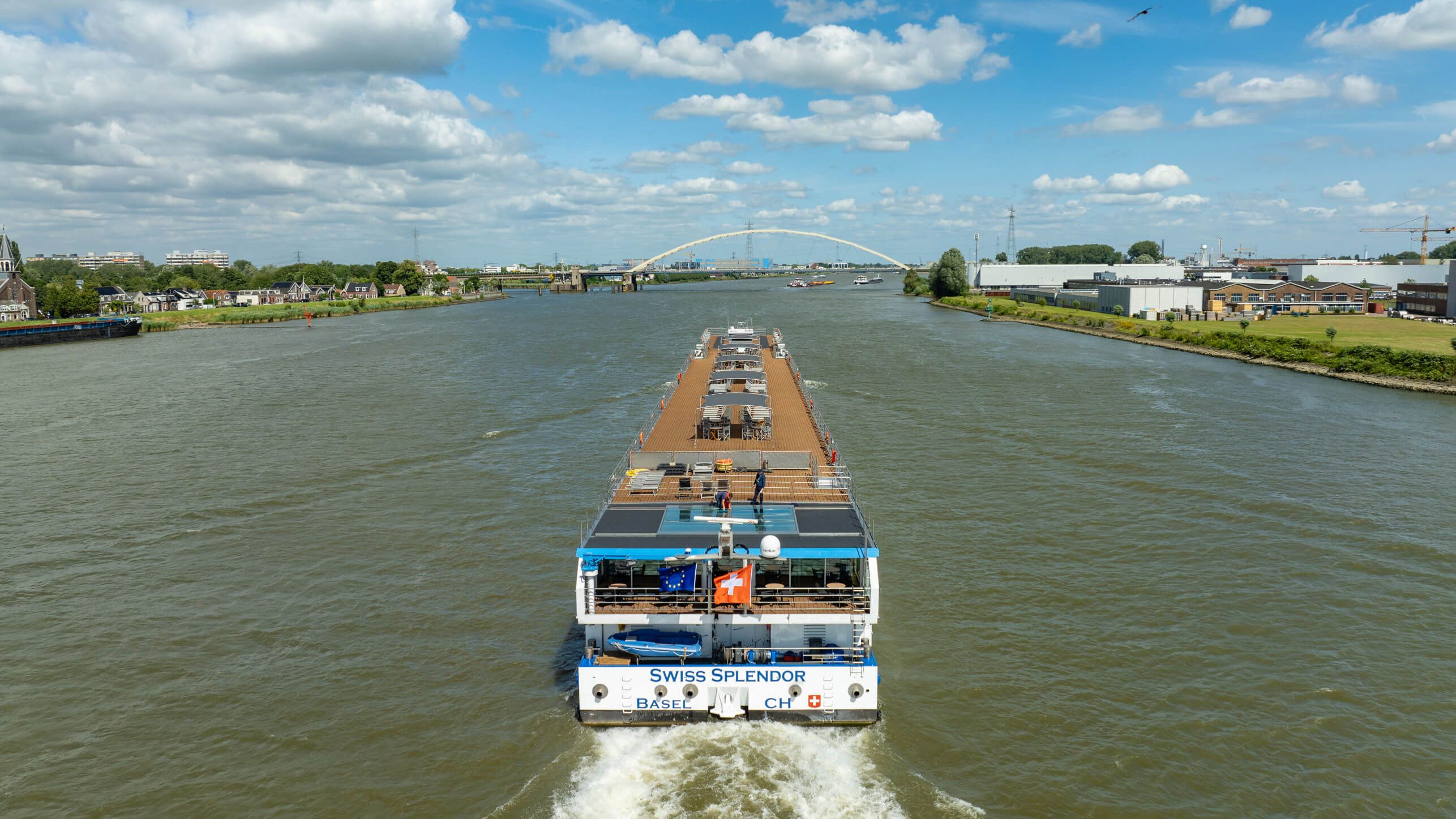 Ein Schiff mit dem Namen „Swiss Splendor“ fährt auf einem Fluss, umgeben von Landschaft und Wolken.