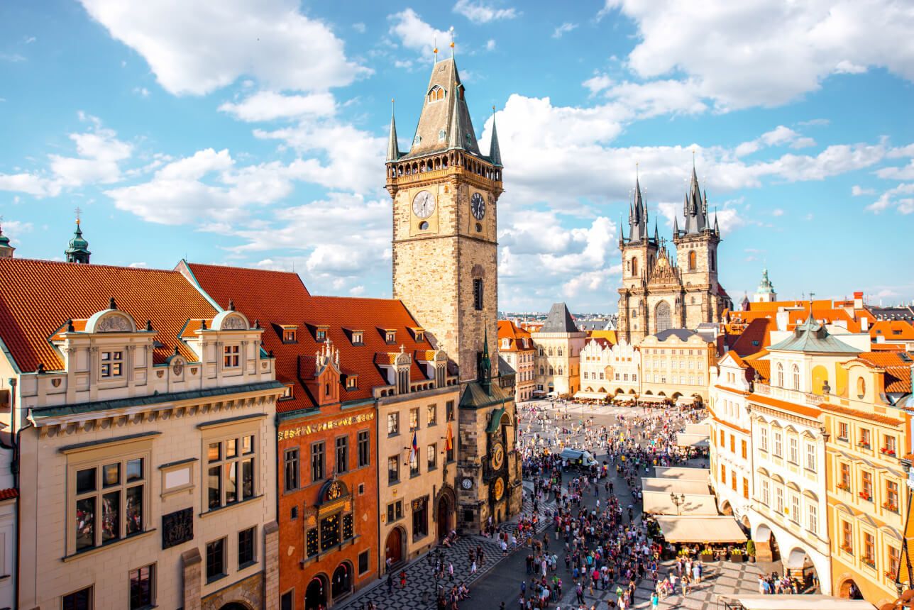 Der historische Marktplatz mit der Astronomischen Uhr und beeindruckenden gotischen Türmen unter blauem Himmel.