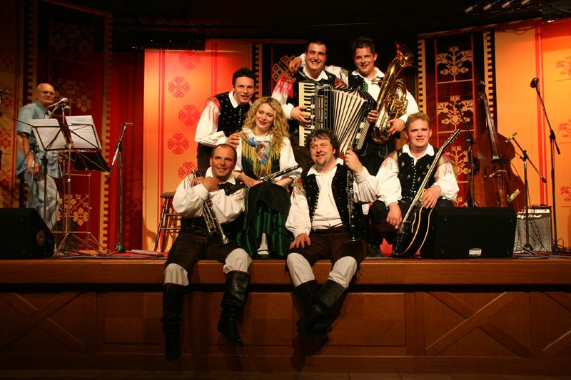 Eine Musikergruppe in traditioneller Tracht posiert mit Instrumenten auf einer Bühnenbühne. Festliche Atmosphäre.