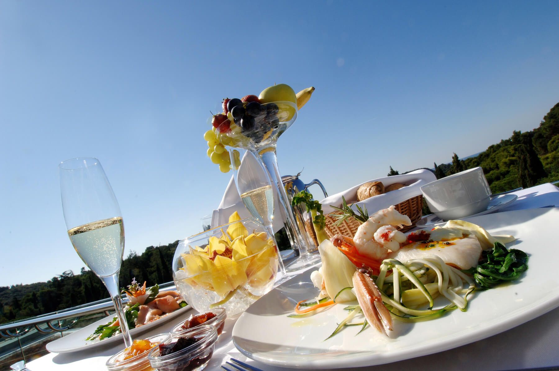 Ein luxuriöses Frühstück mit Meeresfrüchten, frischen Früchten und Sekt, umgeben von klarem Himmel und Natur.