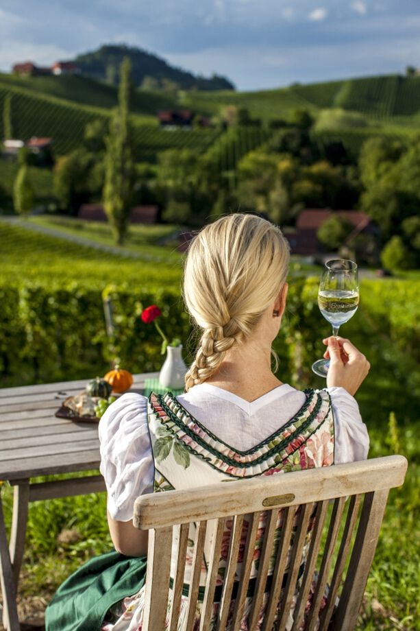 Eine Frau in traditioneller Kleidung genießt Weinblick auf Weinberge und Natur bei schönem Wetter.