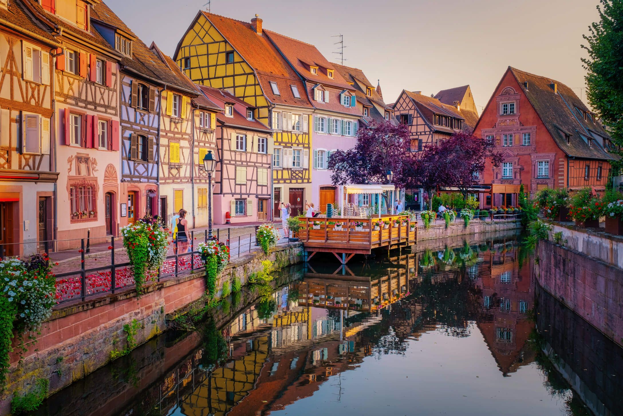 Idyllische Gasse mit Fachwerkhäusern und einem ruhigen Kanal, umgeben von bunten Blumen und Pflanzen.