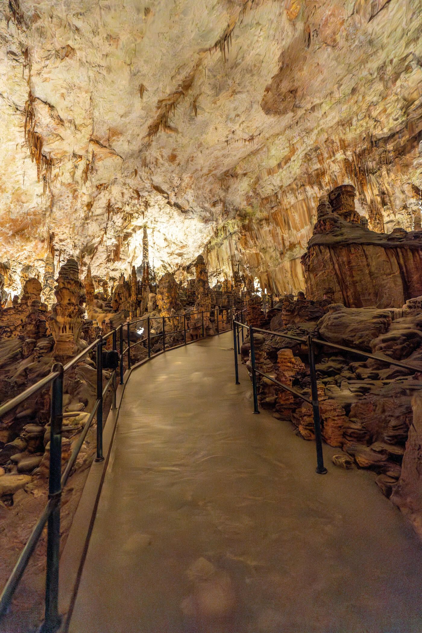 Eine beeindruckende Höhle mit Stalaktiten und Stalagmiten, beleuchtet von warmem Licht auf einem geschwungenen Weg.