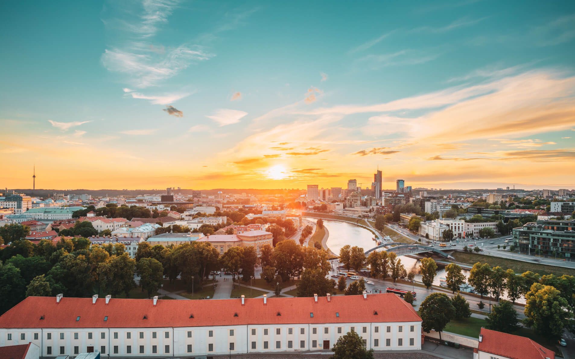 Sonnenuntergang über einer Stadt, Gebäude und Fluss sichtbar, warmes Licht und ein klarer Himmel im Hintergrund.