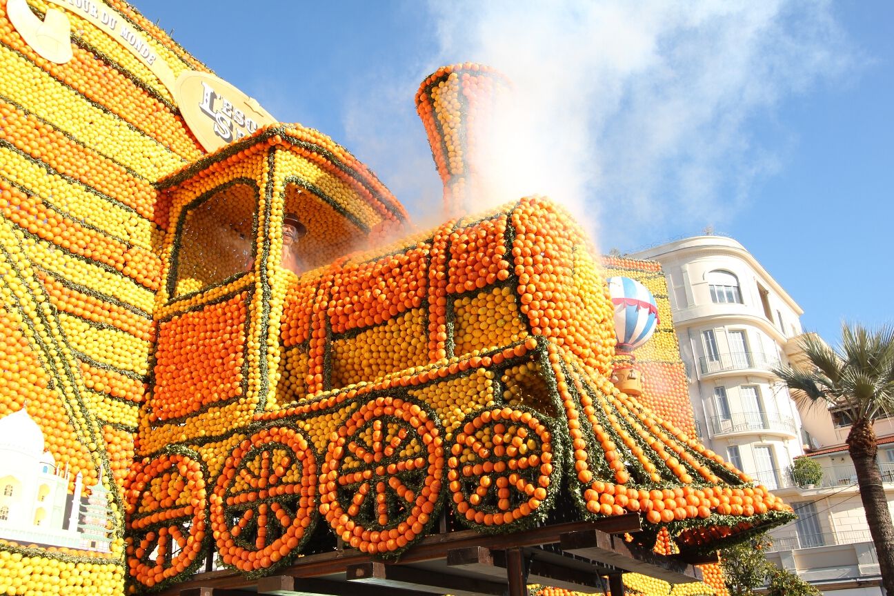 Eine farbenfrohe Lokomotive aus Orangen und Zitronen, umgeben von einem festlichen Ambiente und blauem Himmel.