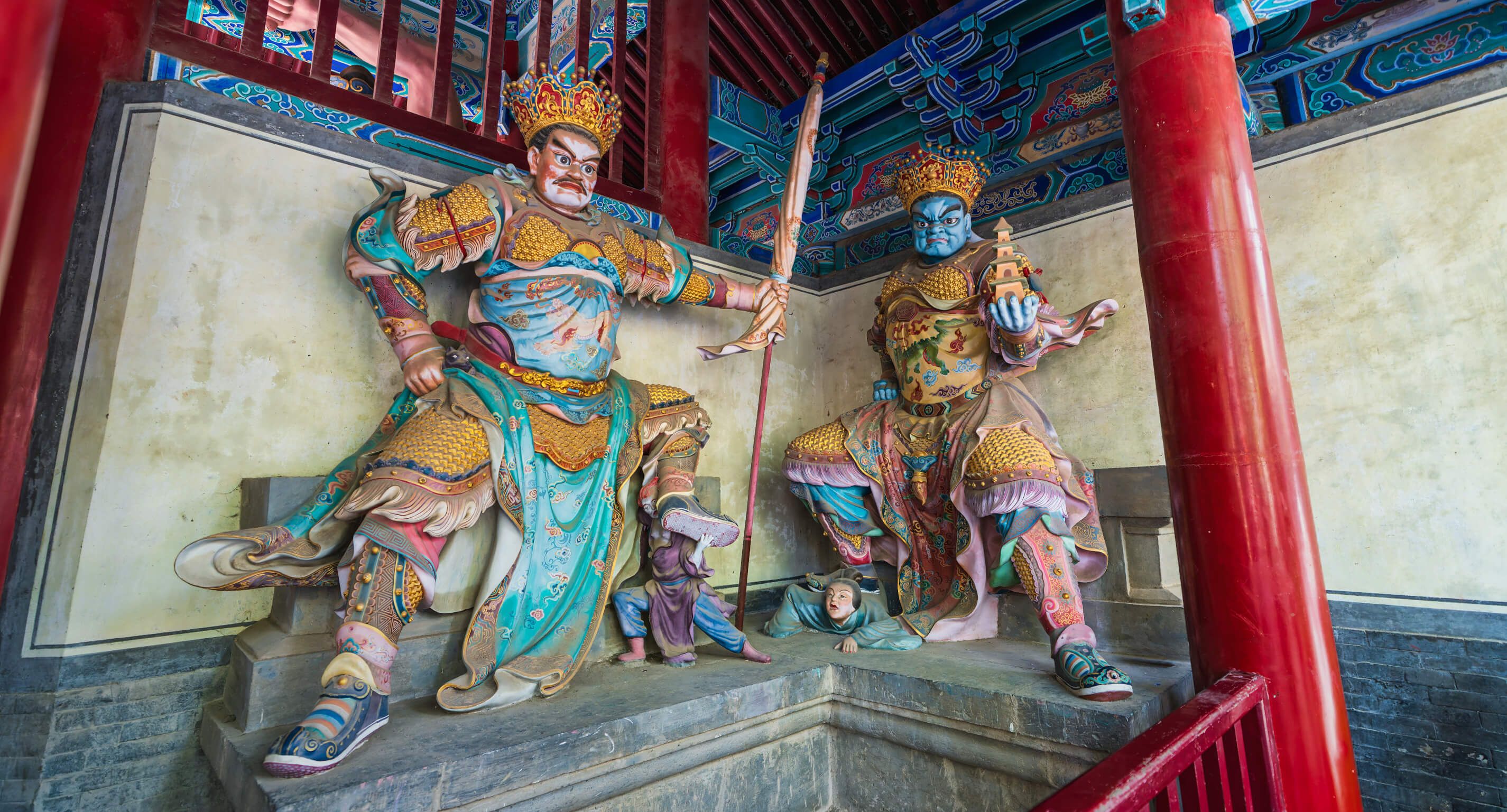 Zwei farbenfrohe Statuen von Wächtern in einem Tempel, umgeben von traditioneller chinesischer Architektur.
