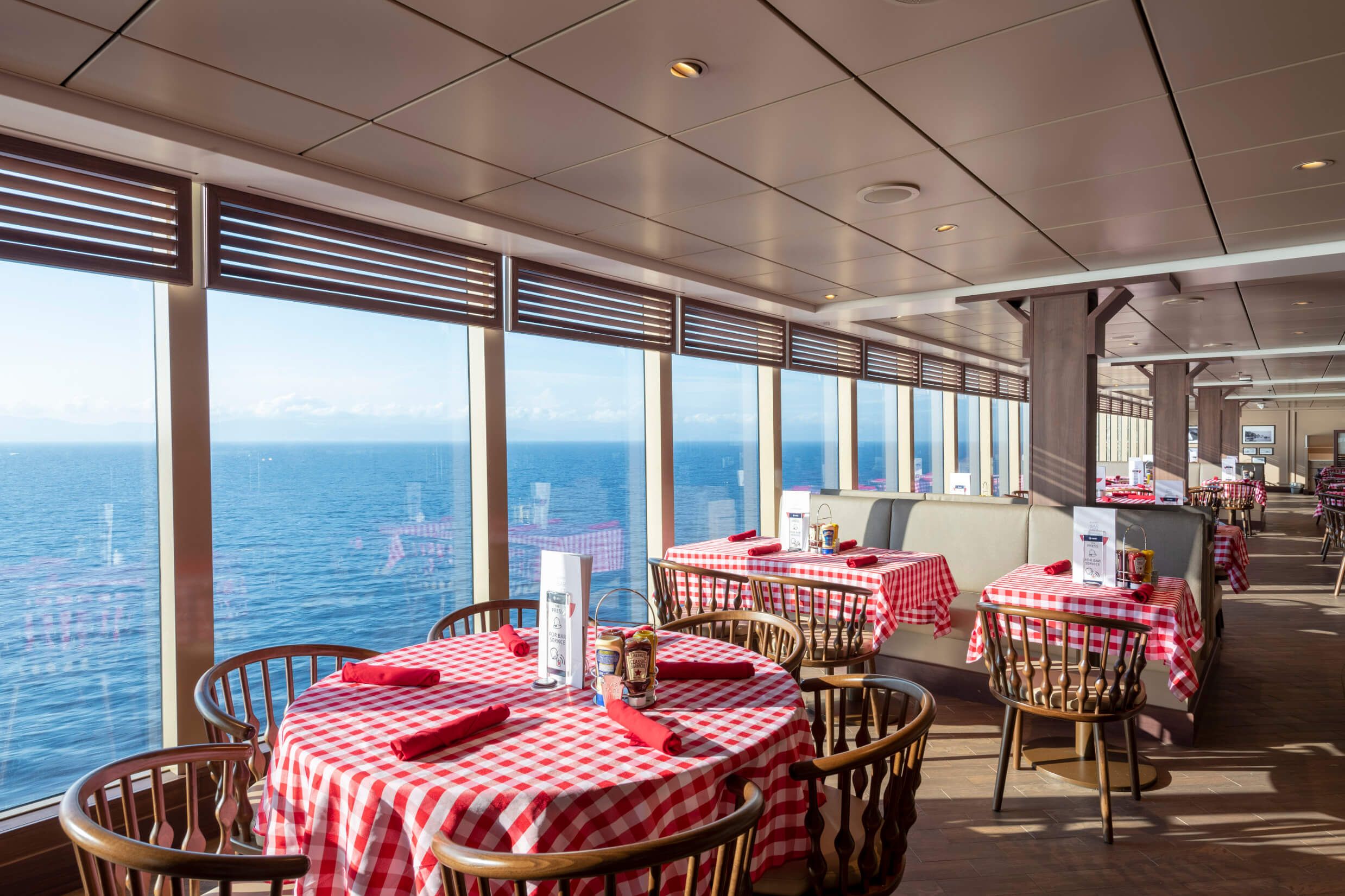 Ein helles Restaurant mit karierten Tischdecken und Meerblick durch große Fenster. Gemütliche Atmosphäre.