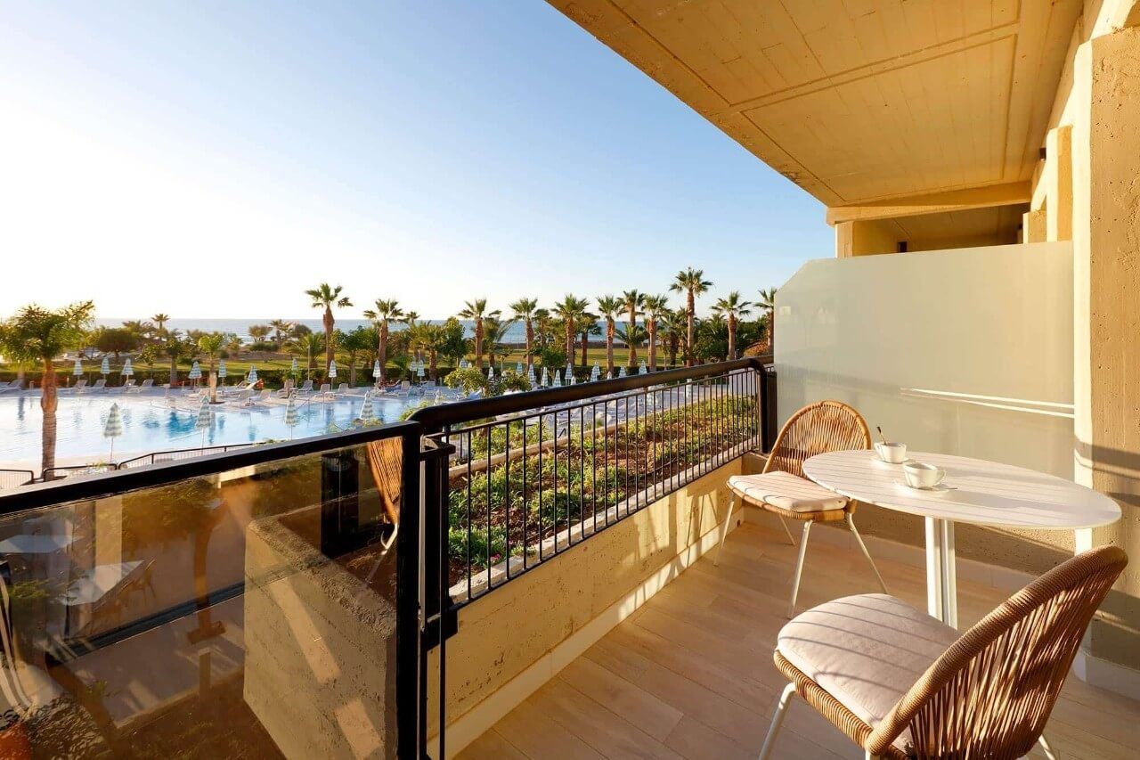 Balkon mit Blick auf den Pool, umgeben von Palmen und Sonne, ideal für entspannende Momente.