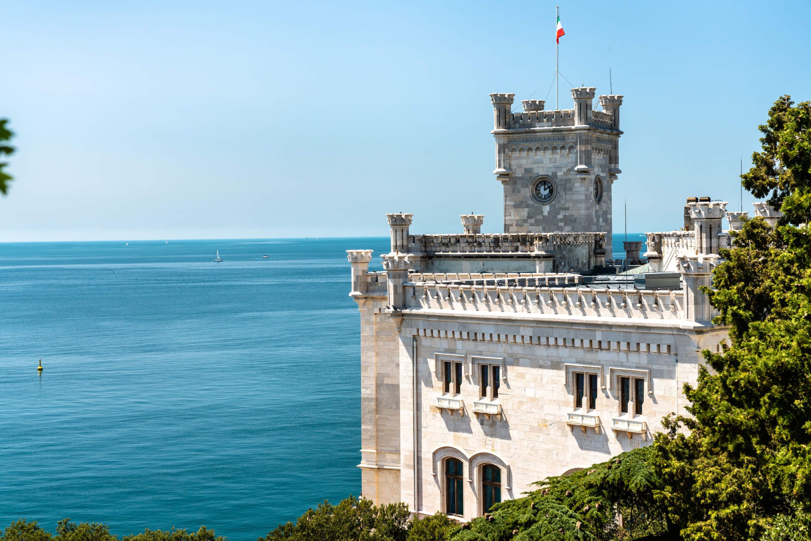 Ein prächtiges historisches Gebäude steht am Meer, umgeben von ruhigem Wasser und blauem Himmel.