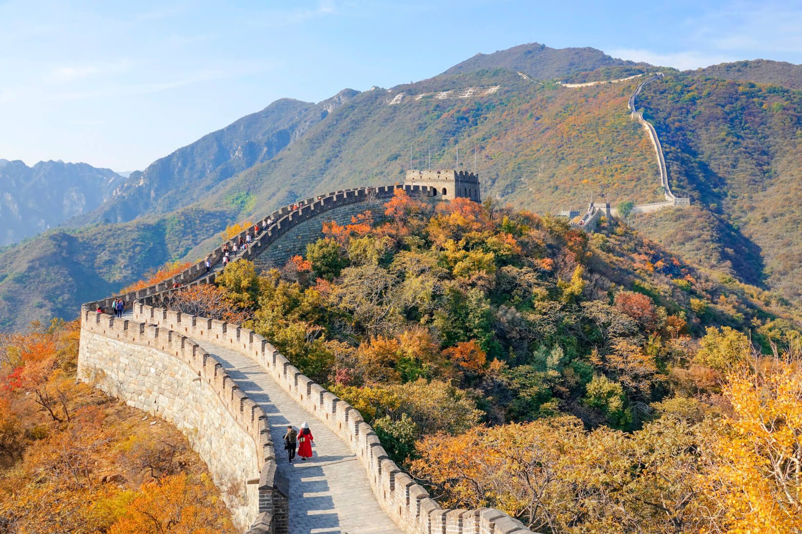 Die Chinesische Mauer schlängelt sich durch herbstliche Landschaften und ist von Besuchern belebt.