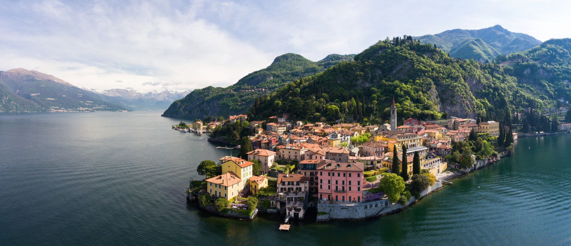 Ein malerisches Dorf am Ufer eines ruhigen Sees, umgeben von üppigen Bergen und klaren Himmel.