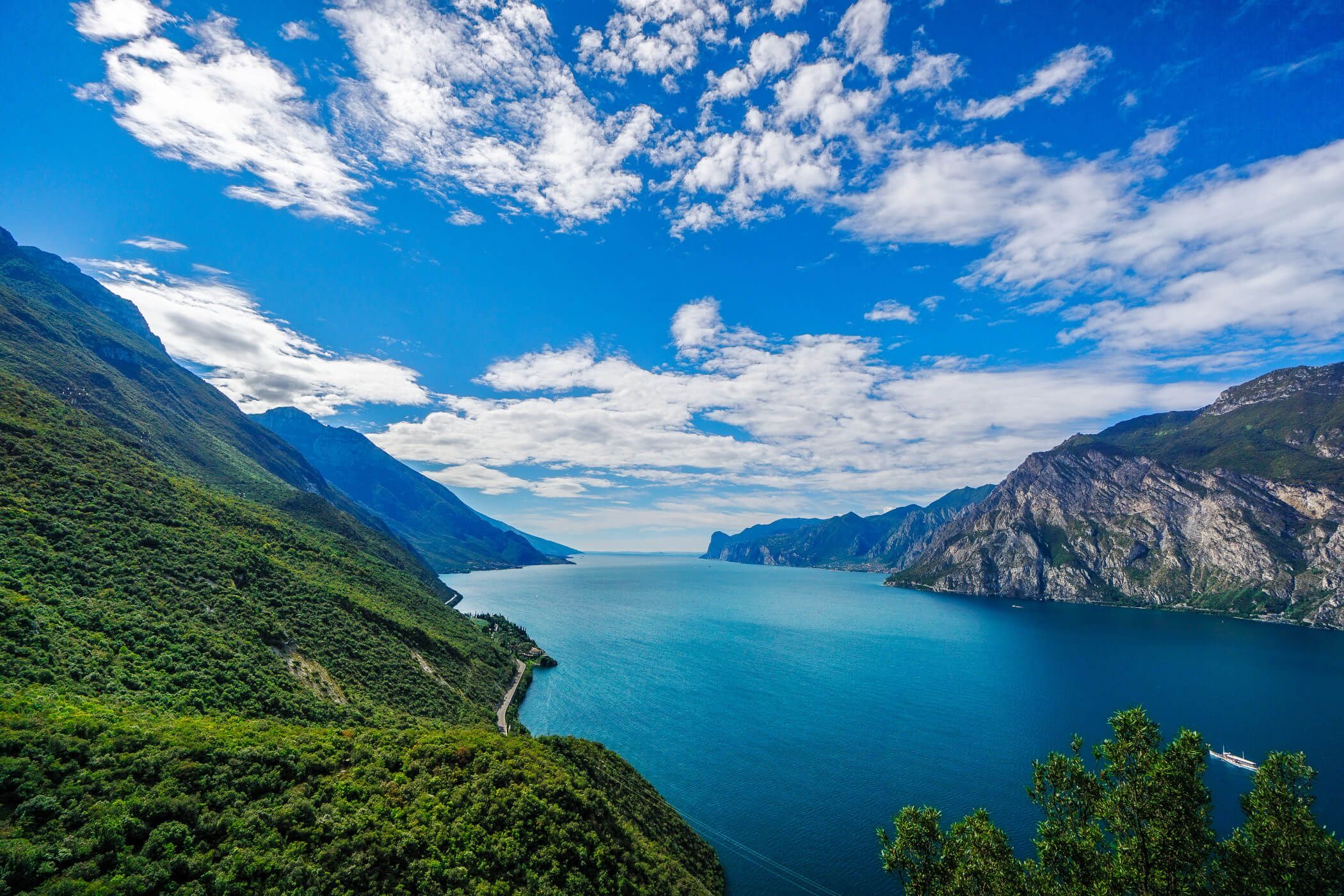 Ein beeindruckender See, umgeben von grünen Bergen und einem strahlend blauen Himmel mit wenigen Wolken.