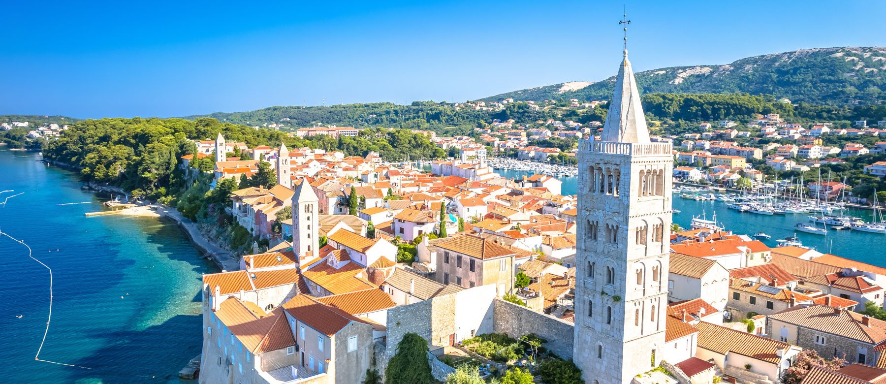 Ein malerischer Blick auf eine Küstenstadt mit bunten Häusern, einem Kirchturm und schönem blauem Wasser.