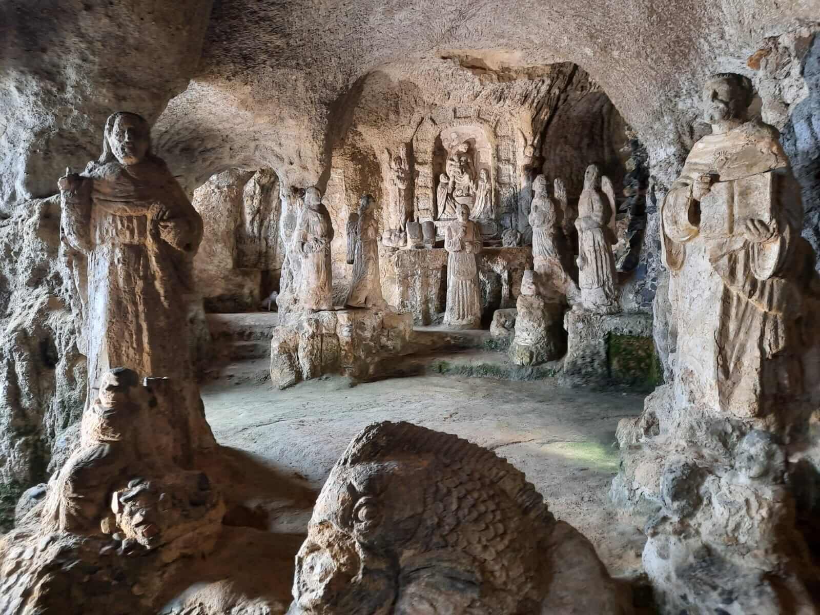 Eine geheimnisvolle Höhle mit kunstvollen Statuen aus Stein, die historische Figuren und Szenen darstellen.