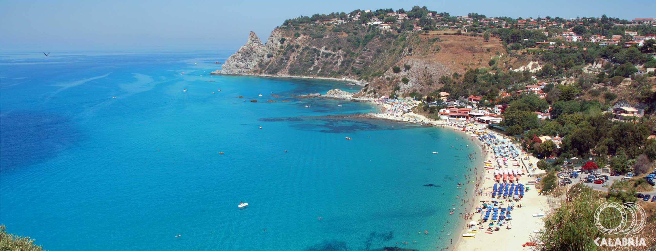 Ein atemberaubender Blick auf den klaren, blauen Strand und die Küste Kalabriens mit Sonnenliegen und Booten.