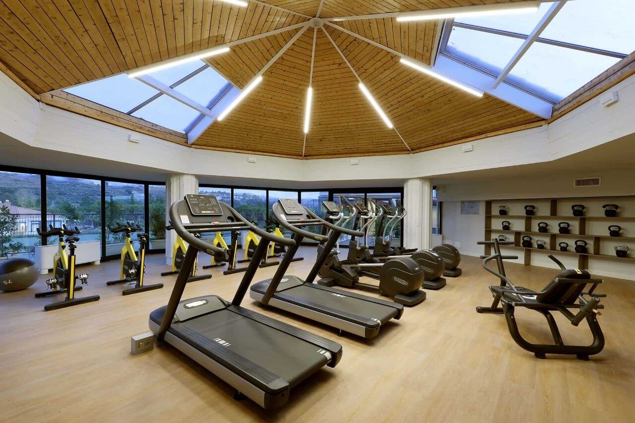 Modernes Fitnessstudio mit Geräten, großen Fenstern und einem einzigartigen Holzdecken-Design.