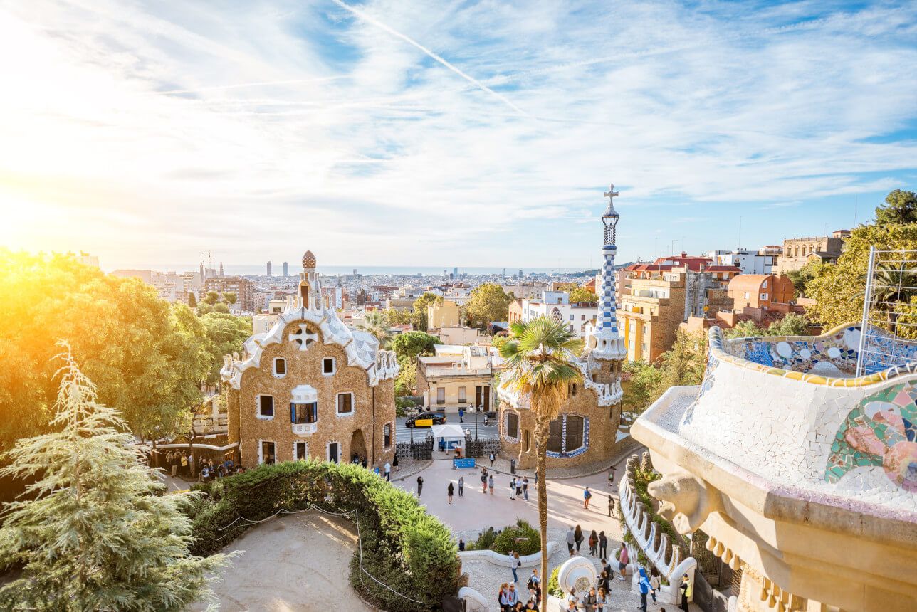Der Park Güell in Barcelona mit bunten Gebäuden, Palmen und einer weiten Aussicht auf die Stadt.
